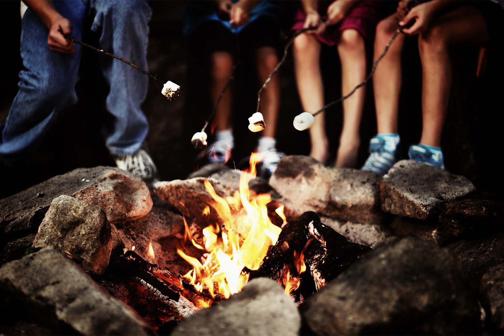 A group of people roasting marshmellows around a campfire.